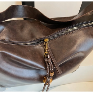 Détail du cabas en cuir marron foncé montrant le zip métallique et le gland tressé