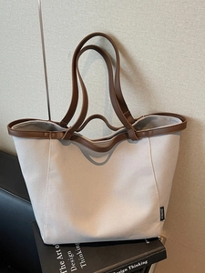 Large canvas tote bag with brown leather trim and handles on a design book base