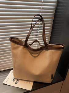 Large khaki canvas tote bag with brown leather trim shown in a natural window setting