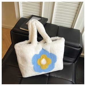 Detail der weißen Plüschtasche mit Sonnenblumenmuster auf schwarzem Ledersofa