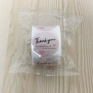 Macro detail of round pink thank you stickers with heart design in roll packaging