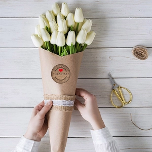 Handmade white tulip bouquet in kraft paper with decorative round labels on white wood