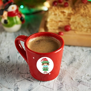 Red ceramic Christmas elf mug filled with coffee on a festive holiday table setting