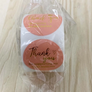 Détail des étiquettes ovales roses avec texte en feuille d'or sous emballage plastique