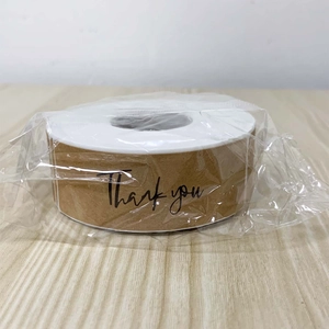 Close-up of kraft paper 'Thank You' stickers in a roll on wooden surface