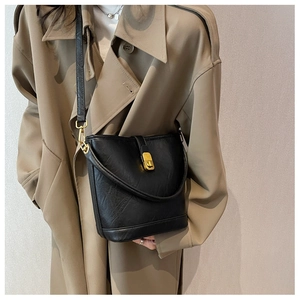 Close-up of black bucket bag with pleated leather texture and gold metal buckle detail