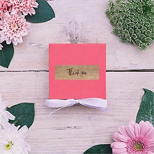 Pink gift box with 'Thank you' kraft sticker and white satin ribbon on wood surface