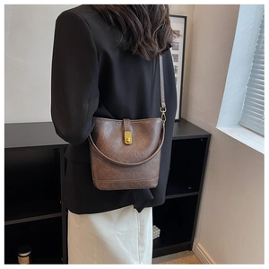 Detail showing deep brown textured bucket bag with golden twist lock and slim strap