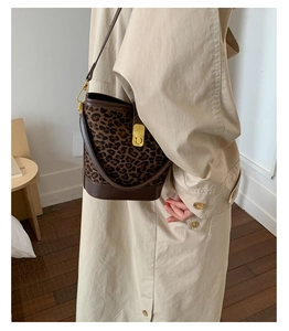 Gros plan du sac seau léopard avec fermoir doré porté sur un trench-coat beige