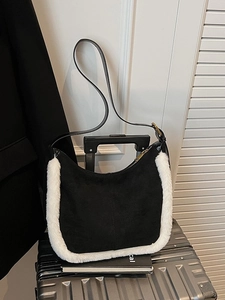 Chic black faux suede underarm bag with white fuzzy trim on a silver suitcase