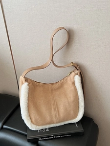 Khaki suede hobo bag with white faux fur trim on a book with soft lighting