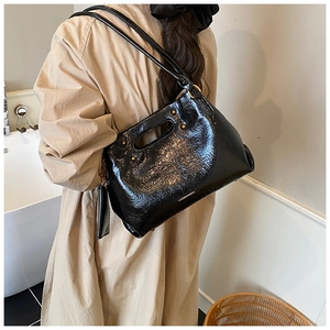 Close-up of black patent leather shoulder bag with gold studs and chain detail