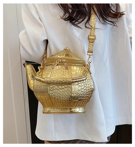 Close-up of golden teapot shape crossbody bag with embossed crocodile texture leather