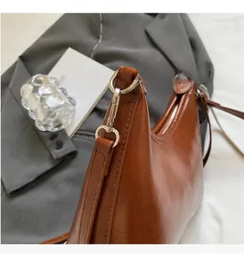 Detail of brown leather crescent bag featuring silver hardware and sleek metal zipper