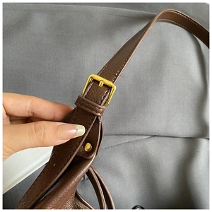 Macro detail of dark brown litchi grain leather strap with gold buckle and stitching
