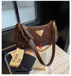 Détail du sac en daim marron avec chaîne dorée et logo triangulaire métallique