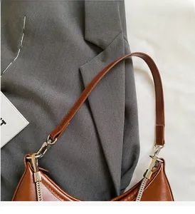 Detail of brown glossy leather shoulder bag showing silver D-ring and chain attachment