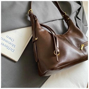 Detail of a brown hobo bag with litchi grain texture on a grey suit jacket