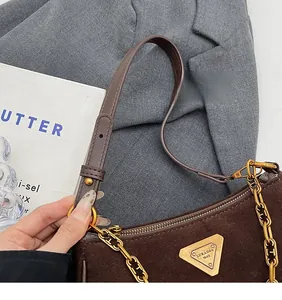 Détail du sac en cuir mat marron foncé avec chaîne dorée et plaque logo triangulaire