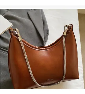 Detail of a brown leather crescent shoulder bag featuring a silver metal chain strap