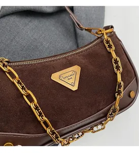 Détail du sac bandoulière en daim marron avec chaîne dorée et plaque en métal triangulaire