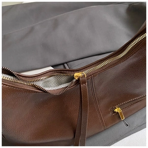 Close-up of brown pebbled leather shoulder bag showing golden zipper and zigzag lining