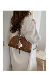 Detail of a brown suede Boston bag with silver eyelet lacing and a baseball charm pendant