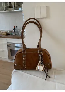 Detail view of brown suede bowling bag featuring metal eyelets and baseball keychain