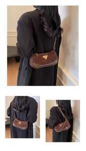 Détail d'un sac bandoulière marron mat avec emblème triangulaire doré et chaîne chic