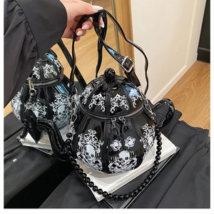 Detail view of glossy teapot shaped handbag with skull pattern and metal chain