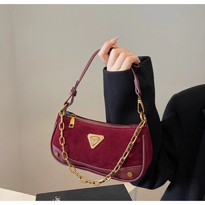 Gros plan du sac bandoulière en daim bordeaux avec chaîne dorée et logo en métal
