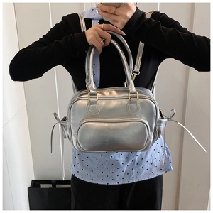 Detail of silver PU leather bag with metallic finish and gold zippers in a tote hand-held view