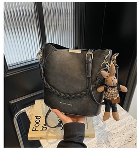 Close-up of black matte bucket bag with a cute rabbit pendant and woven strap detail