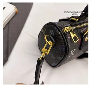 Detail of the golden metal buckle and detachable strap on a black patterned Boston bag