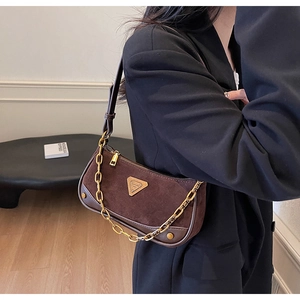 Détail du sac bandoulière en daim marron avec chaîne dorée et logo triangulaire en métal