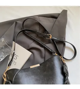 Close-up of black leather handbag with adjustable strap and gold metal buckle detail