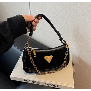 Détail du sac hobo en daim noir avec chaîne dorée et plaque logo triangulaire