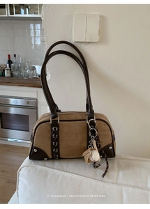 Detail of suede shoulder bag with leather trim and baseball glove charm on white fabric
