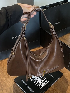 Dark brown leather hobo bag with side tassels and gold hardware on a wooden table