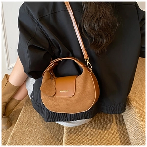 Detail of a brown suede and leather crossbody bag with gold hardware and heart charm