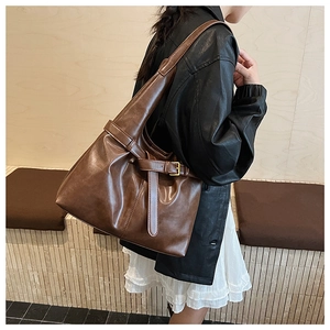 Detail of soft leather tote bag showing crossbody straps and decorative belt buckle