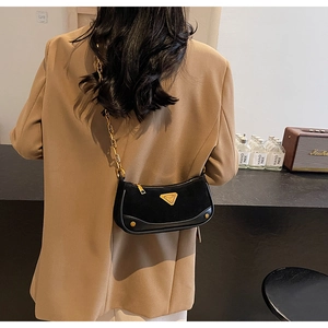 Détail d'un sac en daim noir avec bandoulière chaîne dorée et plaque métal