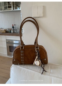 Close-up of retro brown shoulder bag with suede panels, silver studs, and baseball charms