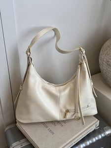 Minimalist beige lychee grain leather hobo bag with gold hardware on a luggage background