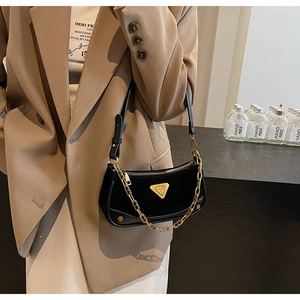 Détail du sac à bandoulière noir mat avec chaîne dorée et emblème logo triangulaire