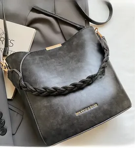 Detail of grey bucket bag showing woven handle and golden logo on textured faux leather