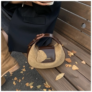 Detail of a half-moon leather handbag with heart charm on a wooden park bench