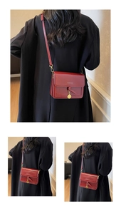 Détail du sac bandoulière bordeaux avec décor de nœud et pendentif doré sur manteau noir