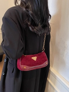 Sac à bandoulière bordeaux avec chaîne dorée porté sur un manteau noir élégant