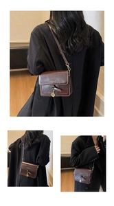Détail d'un sac bandoulière marron vintage avec nœud et pendentif pièce d'or